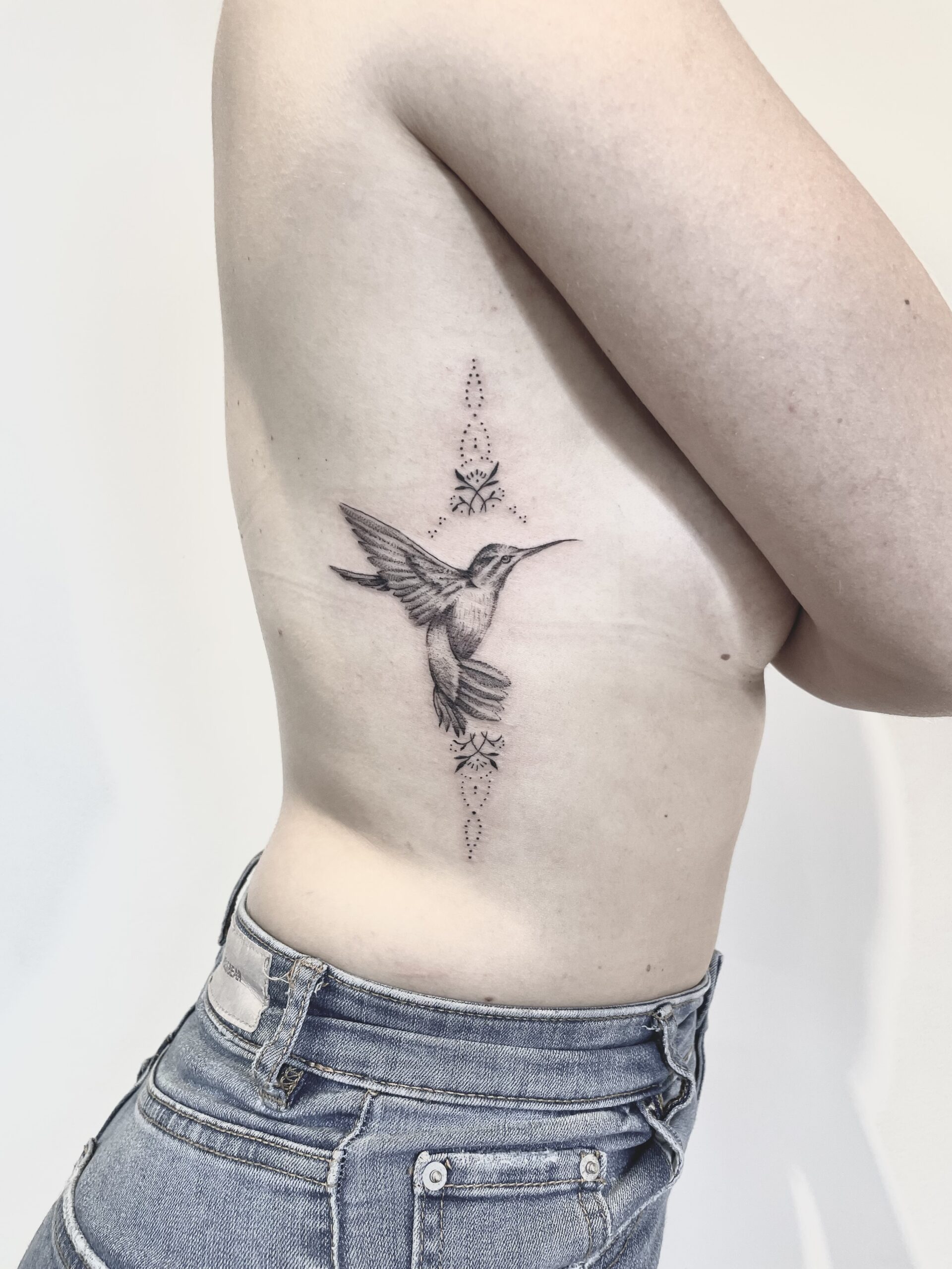 foto von ein kolibri tattoo in fineline stil mit pünkte und ornements auf der Rippen eine junge frau in ein tattoostudio in zürich