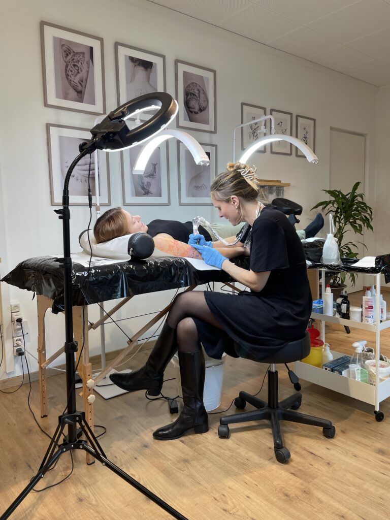 tattoostudio spezialisiert in finelines in zürich, tattooartist am tätowieren, dieses foto zeigt eine tätowiererin bei der arbeit, die tattoo kundin liegt auf eine massage liege und wird am arm tätowiert