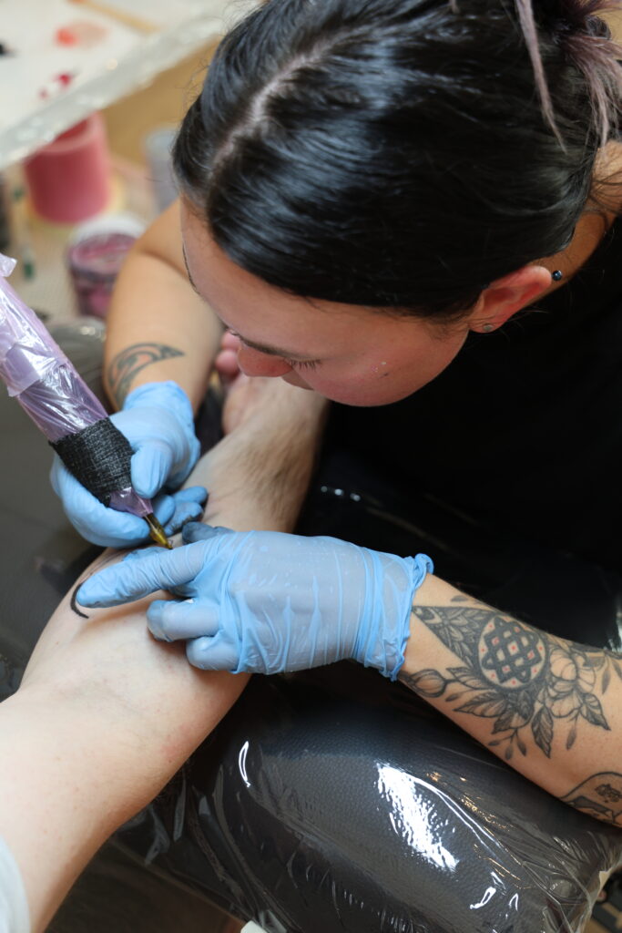 Tätowiererin bei der Arbeit im Amulett Tattoo Studio Zürich – sie tätowiert ein präzises Stencil-Tattoo auf den Arm eines Kunden.